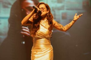 A cantora gospel Daniela Araújo se apresenta em um palco, cantando ao microfone durante um show diante do público.