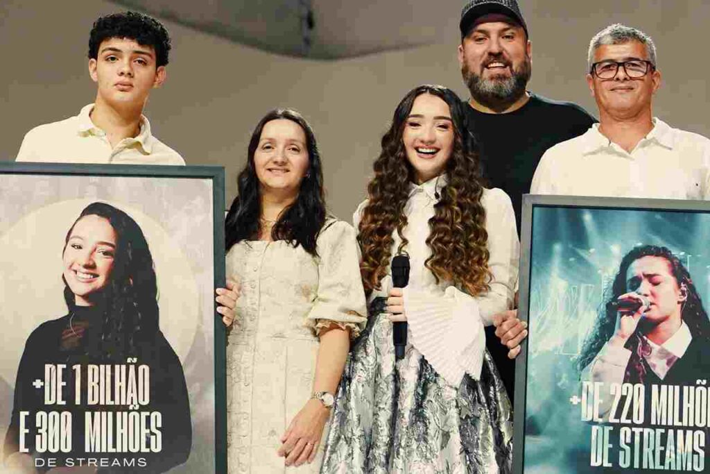 A cantora gospel Kailane Frauches posa ao lado de familiares segurando placas que celebram mais de 1,3 bilhão de streams e mais de 220 milhões de reproduções.