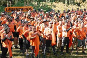 Participantes do movimento Legendários reunidos ao ar livre durante evento de imersão masculina, usando camisetas laranja em área de mata