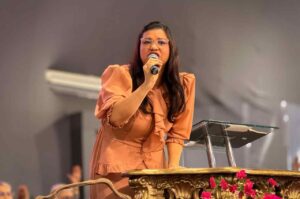 A pregadora Michelle Tito ministra a Palavra em uma igreja, segurando um microfone ao lado do púlpito durante um culto.