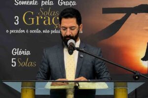 Pastor Bruno Rocha prega atrás do púlpito com a Bíblia aberta, durante uma exposição bíblica sobre as Cinco Solas da Reforma Protestante.