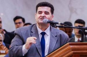 Pastor Edi Viangre prega ao microfone no púlpito de uma igreja durante culto, fazendo um gesto com a mão enquanto ministra a Palavra.