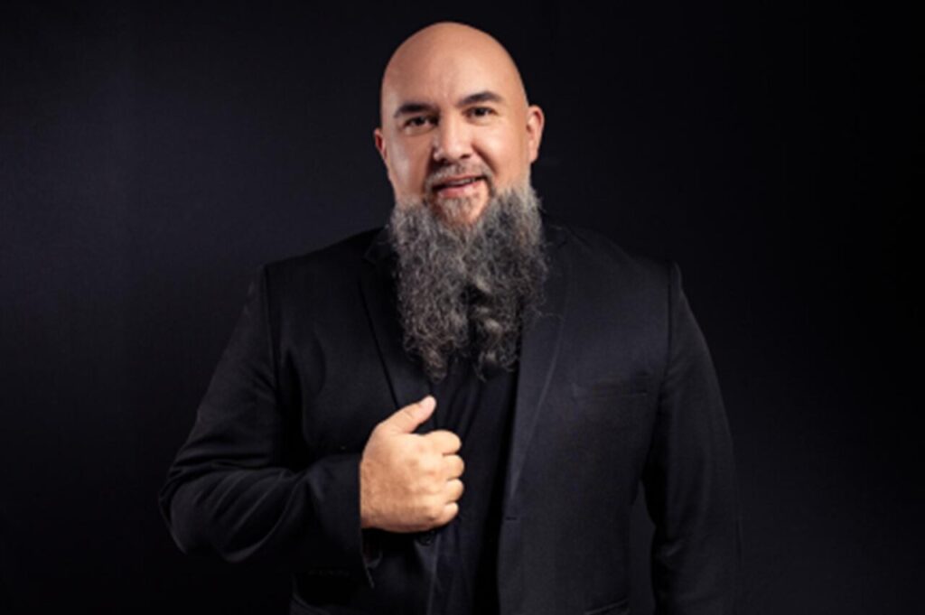 Pastor Wagnão posa para fotografia usando blazer preto sobre fundo escuro.