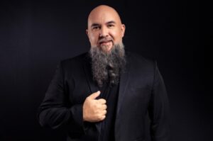 Pastor Wagnão posa para fotografia usando blazer preto sobre fundo escuro.
