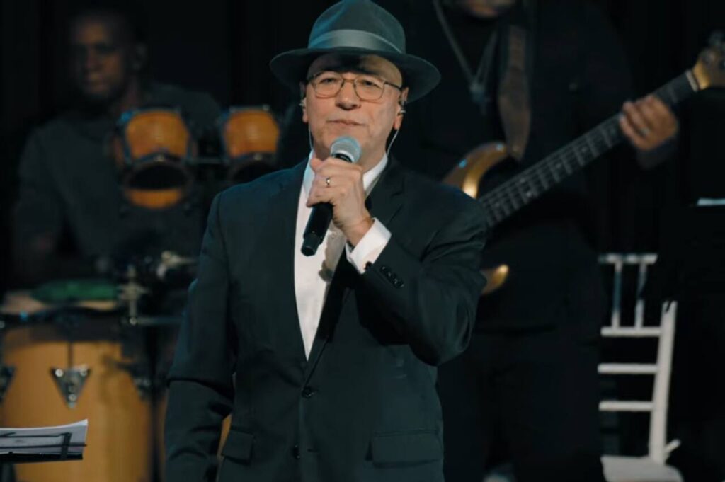 Cantor Sérgio Lopes se apresenta em um palco segurando um microfone durante show.