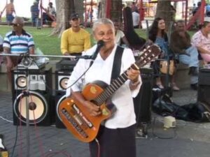 A cantora Creuza de Oliveira canta e toca violão durante uma apresentação ao ar livre em uma praça.