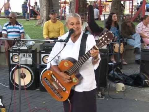 A cantora Creuza de Oliveira canta e toca violão durante uma apresentação ao ar livre em uma praça.