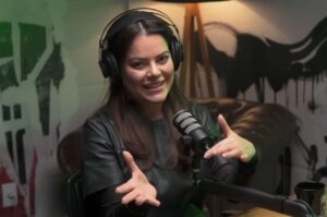 Mulher participa de entrevista em podcast, usando fones de ouvido e falando ao microfone.