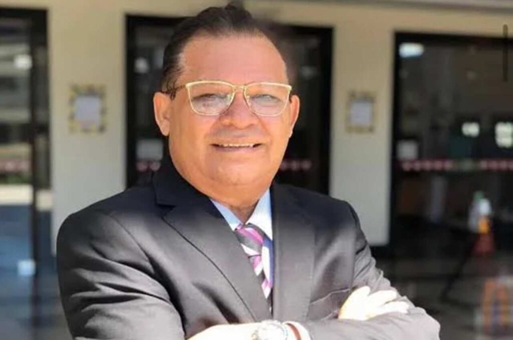 Bispo Francisco de Assis aparece de terno preto e gravata, usando óculos, em frente a um edifício