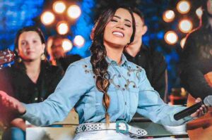 Cantora Stefhany Souza canta durante apresentação ao vivo, segurando um microfone e sorrindo enquanto participa de um momento de louvor.
