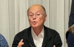 Edir Macedo fala durante entrevista, usando óculos e camisa branca com jaqueta preta.