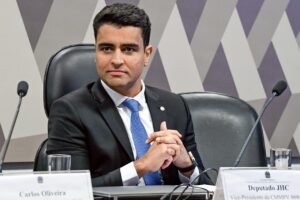JHC aparece sentado durante sessão parlamentar, usando terno preto e gravata azul.