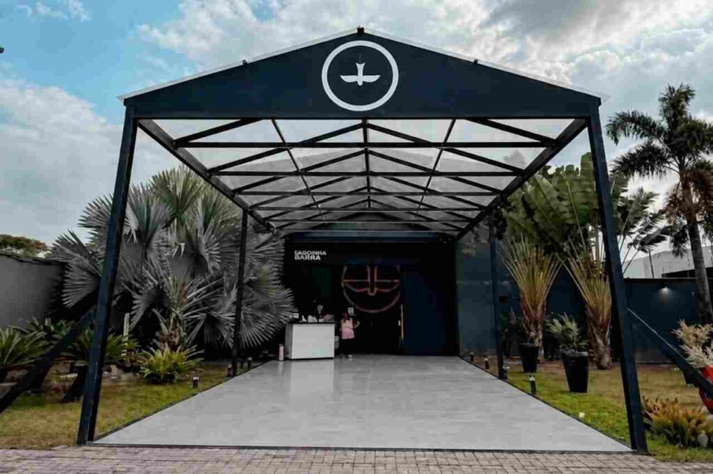 Fachada da Igreja Lagoinha Barra, com entrada coberta, jardim e logomarca da igreja.