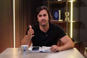 Pastor Pyero Tavolazzi fala diante da câmera com uma Bíblia aberta sobre a mesa.