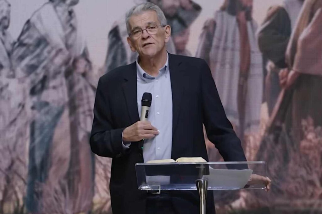 Pastor Elias Dantas prega segurando um microfone diante de um púlpito com a Bíblia aberta.