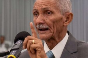 : Pastor José Carlos de Lima prega ao microfone com o dedo indicador levantado durante culto em igreja evangélica.