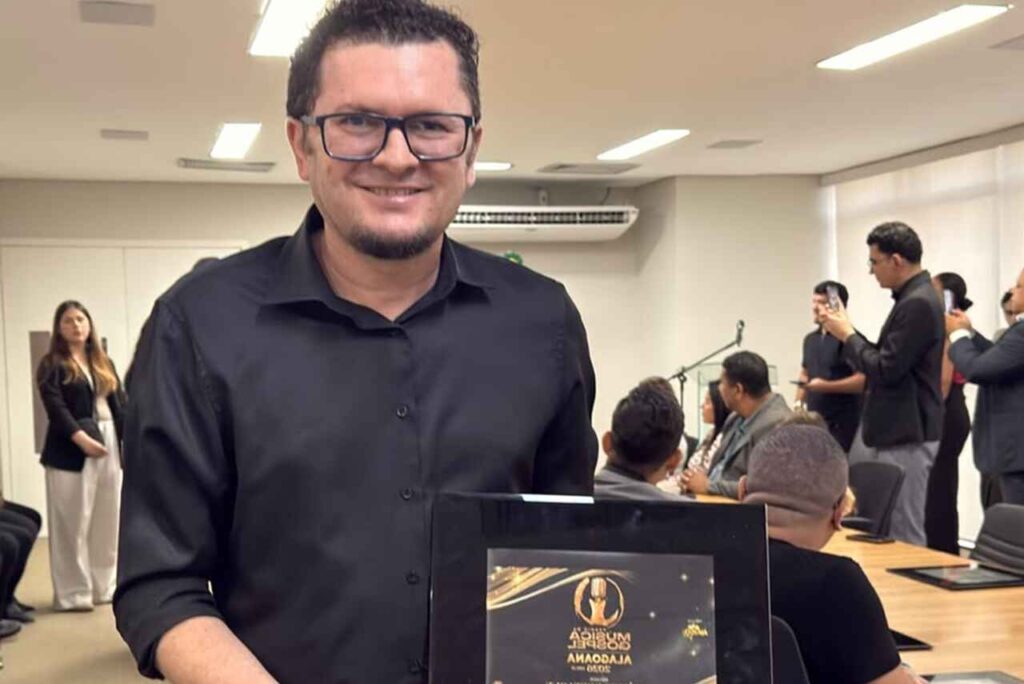 Saxofonista Oziel Melo posa segurando uma placa de reconhecimento durante evento.