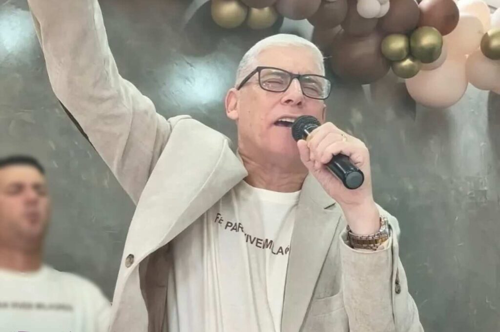 Pastor Sérgio Sora canta ao microfone durante culto.