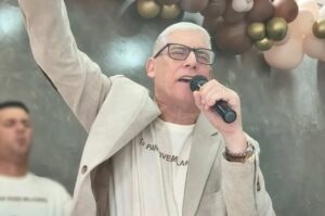 Pastor Sérgio Sora canta ao microfone durante culto.