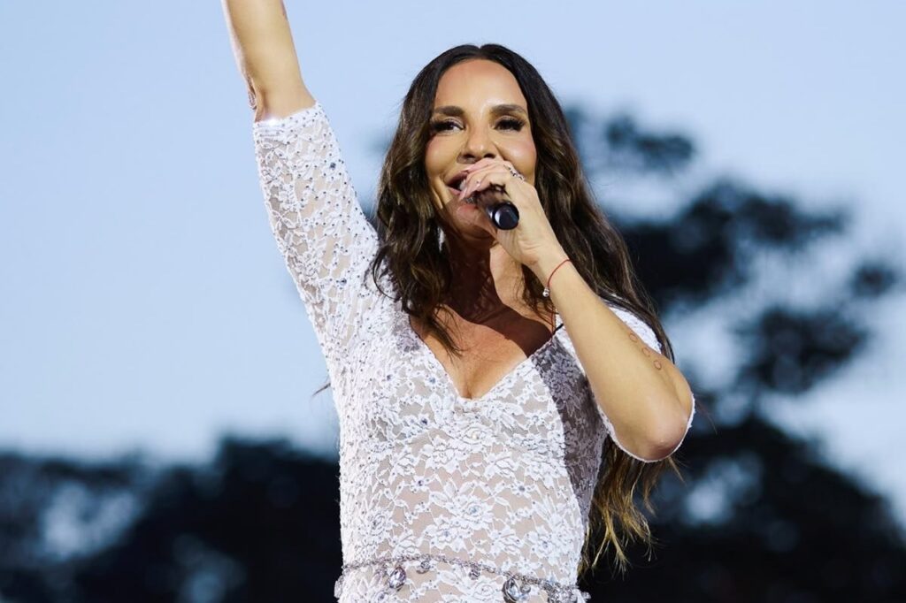 Ivete Sangalo canta ao vivo com microfone e braço levantado durante apresentação musical