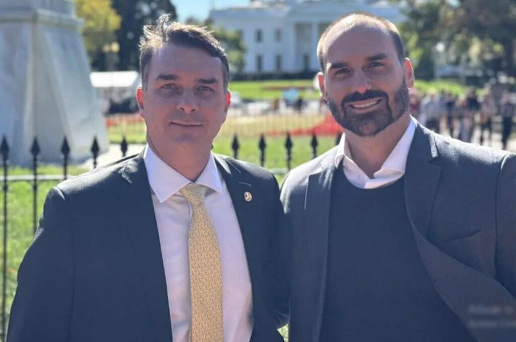 Flávio Bolsonaro e Eduardo Bolsonaro aparecem juntos em fotografia ao ar livre, usando ternos e gravatas em frente a um edifício público.