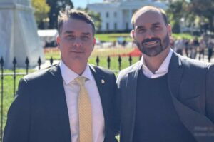 Flávio Bolsonaro e Eduardo Bolsonaro aparecem juntos em fotografia ao ar livre, usando ternos e gravatas em frente a um edifício público.