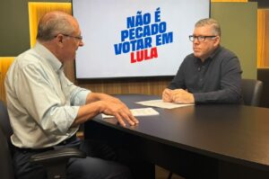 Geraldo Alckmin e o pastor Ed René Kivitz conversam sentados à mesa, diante de uma tela com a frase “Não é pecado votar em Lula”.