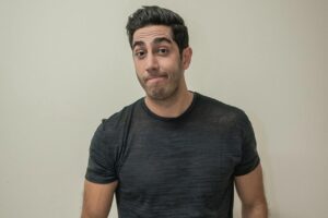 Humorista Jonathan Nemer posa para fotografia usando camiseta preta, com expressão descontraída e fundo neutro claro.
