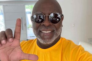 Kleber Lucas posa para selfie com óculos escuros redondos e camiseta amarela, fazendo sinal com a mão.