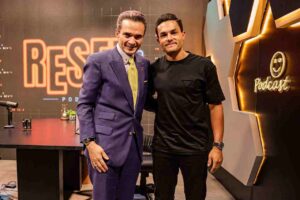 Samuel Ferreira, de terno roxo e gravata amarela, conversa com David Miranda Neto, que veste camiseta preta, durante encontro em ambiente interno.